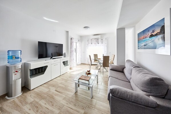 A modern living room with a flat-screen TV, a water dispenser, a glass coffee table, and a grey sofa. - Penthouse with Sea View (Benidorm)