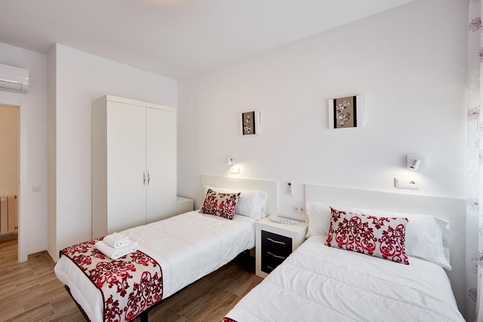 Een hotelkamer met twee bedden, een kledingkast, nachtkastjes en een wandlamp.
