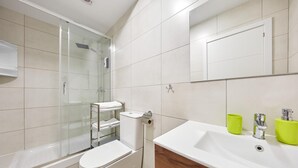 A modern bathroom with a glass shower enclosure, a toilet, a sink with a mirror, and a vanity with a wooden cabinet. - Deluxe Studio Apartment 100 meters from the beach (Benidorm)