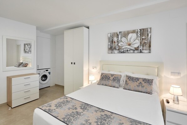 A bedroom with a bed, a dresser, a washing machine, and a large mirror.