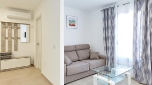 Een moderne woonkamer met een beige bank, een glazen salontafel en een groot raam met patroon gordijnen.
