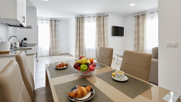 Ein moderner Essbereich mit einem für das Frühstück gedeckten Tisch, darunter Croissants, eine Obstschale und eine Kaffeetasse.