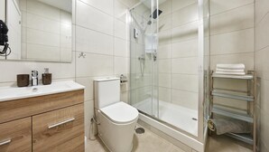 Ein modernes Badezimmer mit einer Duschkabine, einer weißen Toilette, einem Waschtisch mit Spiegel und einem Handtuchhalter.