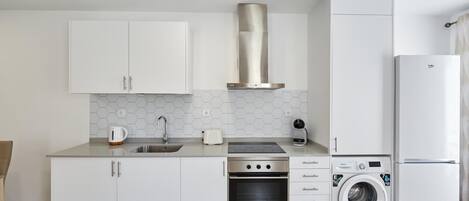 A modern kitchen with white cabinets, a stainless steel range hood, a built-in oven, a washing machine, and a refrigerator.
