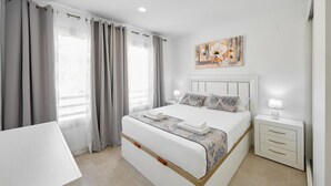 Ein modernes Schlafzimmer mit einem großen Bett, einem Nachttisch mit Lampe und einem Bild an der Wand.