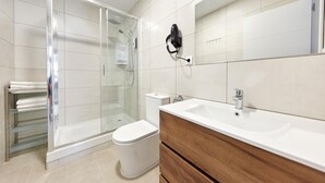 Een moderne badkamer met een douchecabine van glas, een wit toilet, een wastafel met spiegel en een handdoekrek.