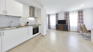 Een moderne keuken met witte kastjes, een roestvrijstalen spoelbak en een inbouwoven. Er is een eethoek met een televisie en een eettafel.