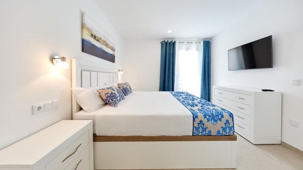 Een moderne slaapkamer met een bed, nachtkastjes, een televisie en een schilderij aan de muur.