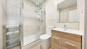 Een moderne badkamer met een douchecabine van glas, een wit toilet, een houten wastafelmeubel met een wastafel en een spiegel erboven.