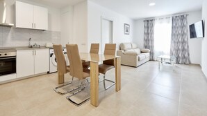 Een moderne keuken met witte kastjes, een inbouwoven, en een eethoek met een glazen tafel en bruine stoelen.