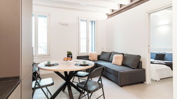 A modern living space with a round dining table, grey sofa, and a bed with a white bedspread. - Suite JOIVY Lake 11 (Como)