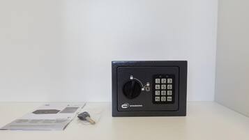 A black safe with a keypad and a keyhole, placed on a white surface with documents and a keychain nearby.