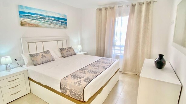 A bedroom with a large bed, a nightstand, a bedside table, a vase, and a painting on the wall. - Deluxe Apartment 100 meters from the beach (Benidorm)