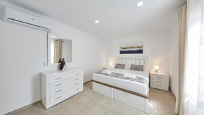 Une chambre à coucher moderne avec un grand lit, une commode, un miroir et un tableau accroché au mur.
