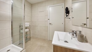 Une salle de bain moderne avec une douche à parois de verre, un lavabo blanc avec un meuble en bois, et un porte-serviettes avec des serviettes pliées.