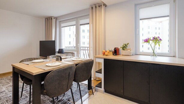 A modern kitchen with a dining area, large windows, and a view of the city. - ShortStayPoland Bohaterewicza B174 (Warsaw)