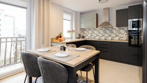 A modern kitchen with dark cabinets, a microwave, and a stove. There is a dining table with chairs and a window with curtains. - ShortStayPoland Bohaterewicza B174 (Warsaw)