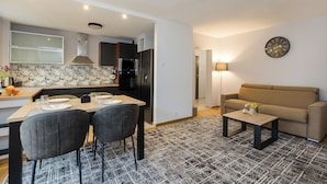 A modern living room with a sofa, a coffee table, and a dining area with chairs and a table set for four. - ShortStayPoland Bohaterewicza B174 (Warsaw)