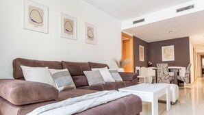 Un salon moderne avec un canapé en cuir marron, une table basse blanche et un coin repas doté de chaises à motifs.