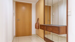 Un couloir avec une porte en bois, un meuble avec une porte-miroir et un sol carrelé.