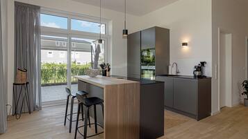 A modern kitchen with a central island, bar stools, and a view of the outside.