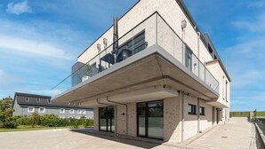 Un edificio moderno de dos pisos con balcón, ventanas amplias y techo plano.