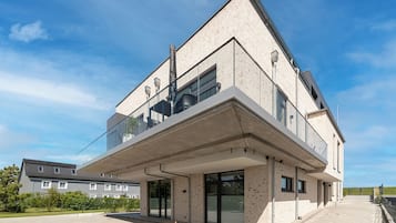En moderne bygning med to etager, balkon, store vinduer og et fladt tag.