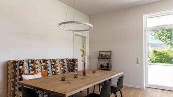 Un coin repas avec une table en bois, des chaises noires, un banc à motifs, un vase de fleurs et une vue à travers une porte vitrée.