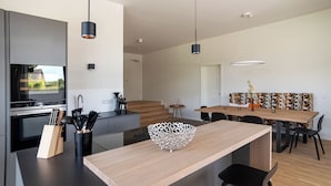 Una cocina moderna con una isla central, lámparas colgantes negras y un comedor con mantel estampado.