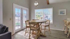 A dining area with a round wooden table and four chairs, a chandelier, and a view through a window with blinds. - Steps to bay & ocean, Belmont Park, A/C family fun (San Diego)