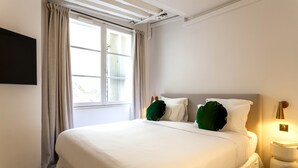 Un letto rifatto con lenzuola bianche e cuscini verdi, una lampada da comodino e una finestra con tende.