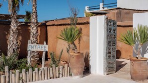 A sign reading "ENTREE" in front of a building with a rustic exterior and palm trees. - La Mouette et les Dromadaires (Essaouira)