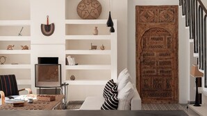 A modern living room with a white sofa, a coffee table, and a TV. There are shelves with decorative items and a large wooden door. - La Mouette et les Dromadaires (Essaouira)
