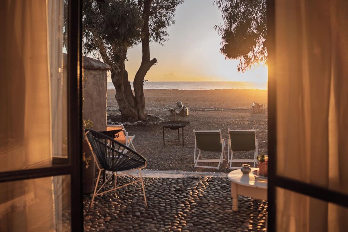 A beach view from inside a room with a stone floor, two chairs, a table, and a fire pit.