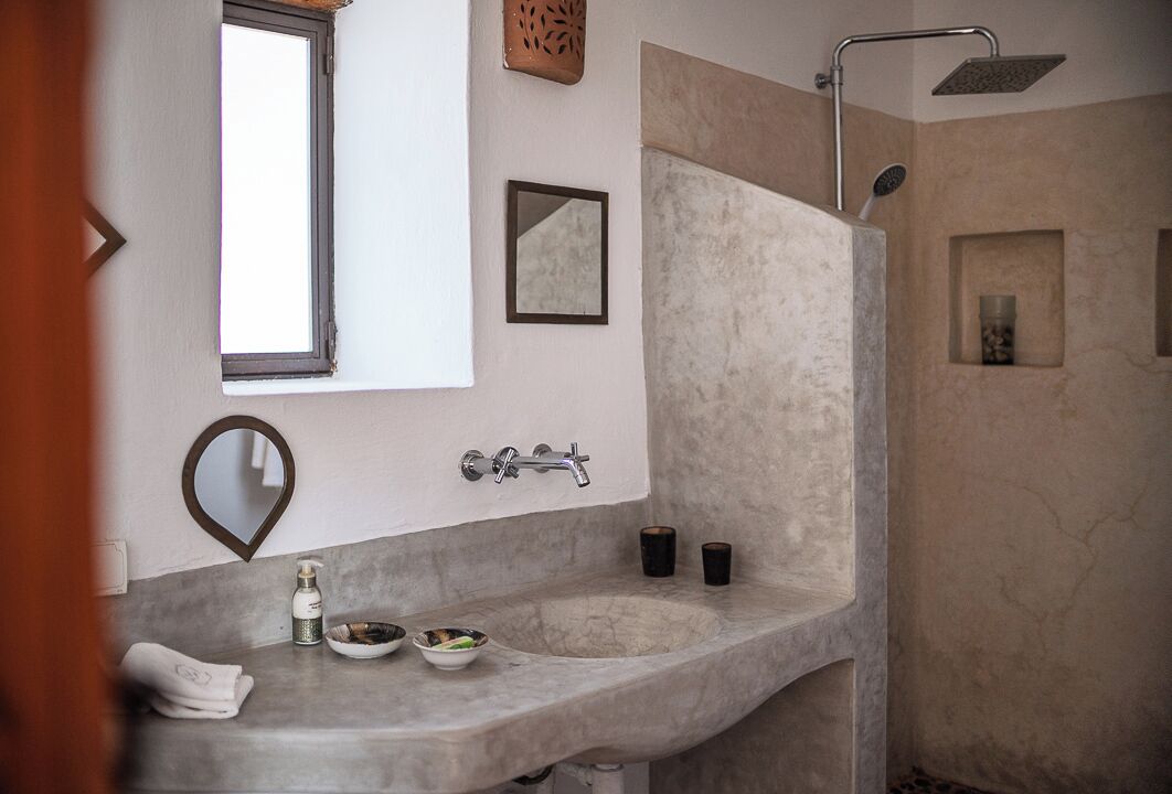 A bathroom with a large sink, a mirror, a shower, and a small shelf with candles.