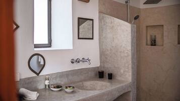 A bathroom with a large sink, a mirror, a shower, and a small shelf with candles.