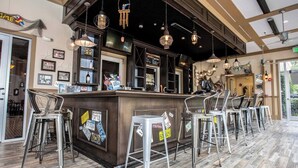 Zona de bar con mostrador de madera y taburetes metálicos, destacando una decoración rústica con luces colgantes e imágenes enmarcadas.