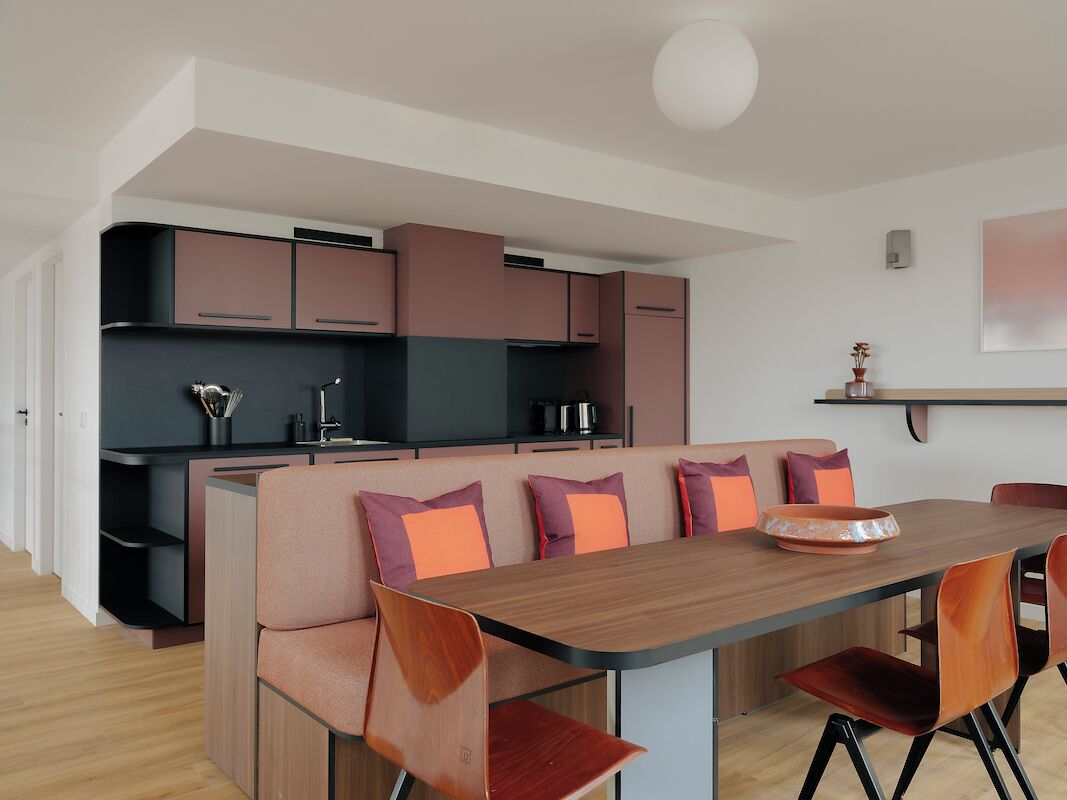 A modern kitchen with built-in appliances, a dining area with a wooden table and orange chairs, and a kitchen island with seating.