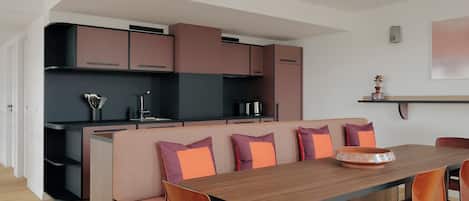 A modern kitchen with built-in appliances, a dining area with a wooden table and orange chairs, and a kitchen island with seating.