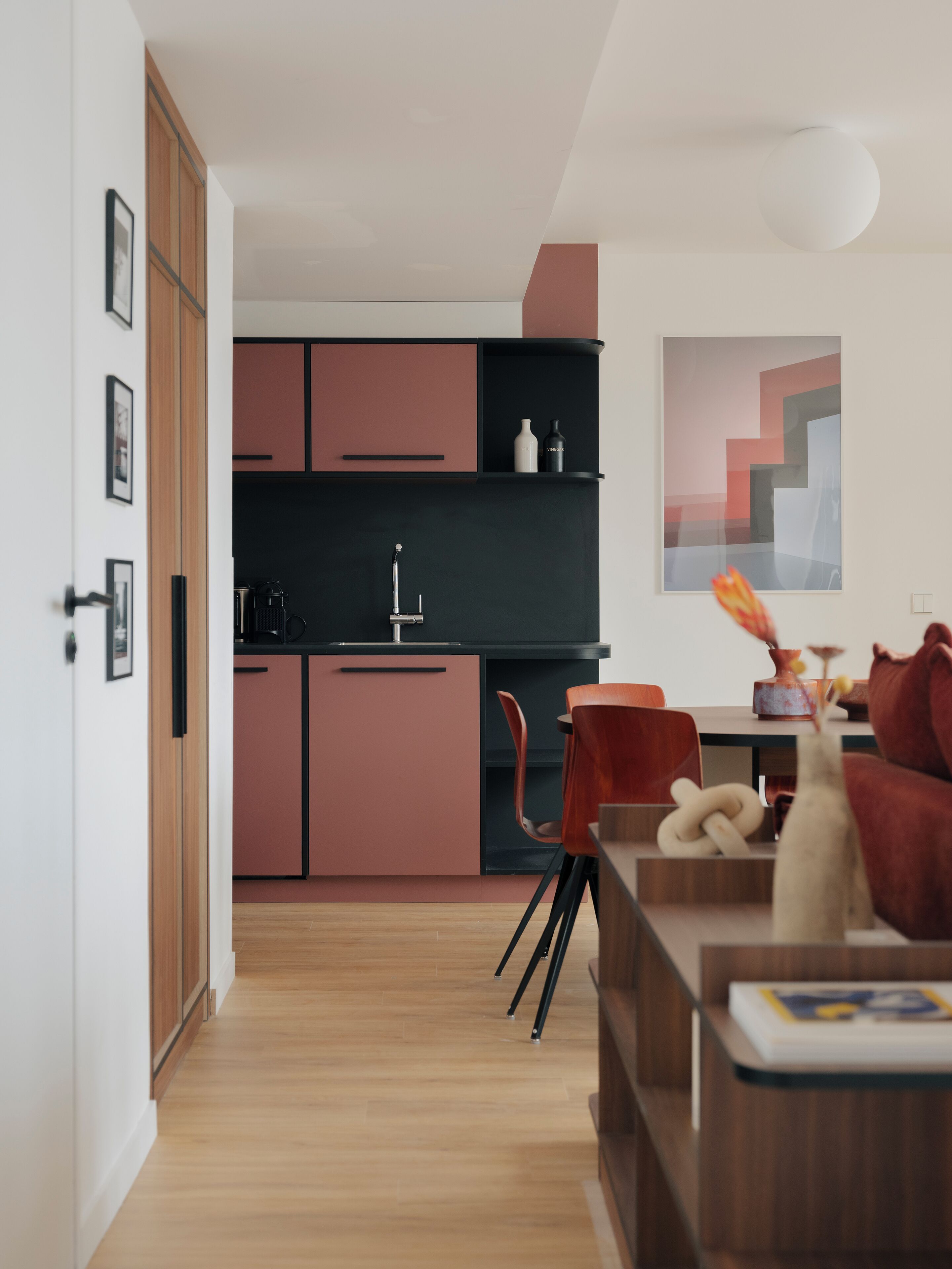 Una cocina moderna con una isla central, armarios de madera y un comedor con una silla roja y una mesa.
