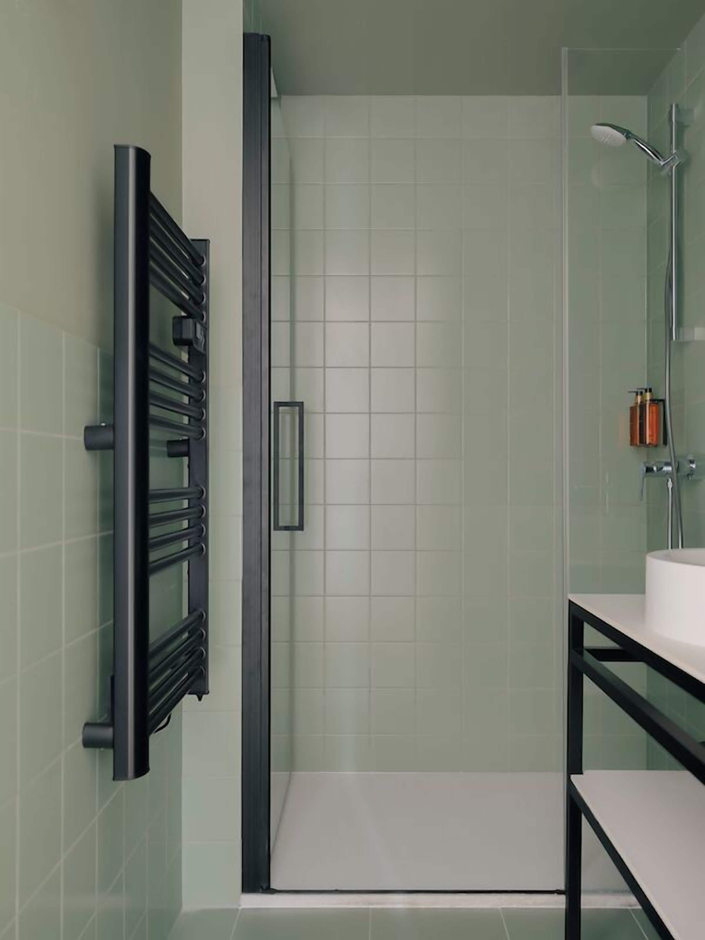 A modern bathroom with a glass shower enclosure, a black towel rack, and a white sink.