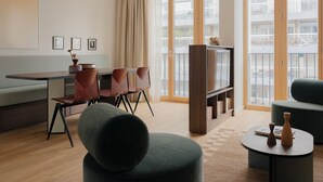 Un salon moderne avec un canapé, des fauteuils, une table à manger, un téléviseur et de grandes fenêtres.