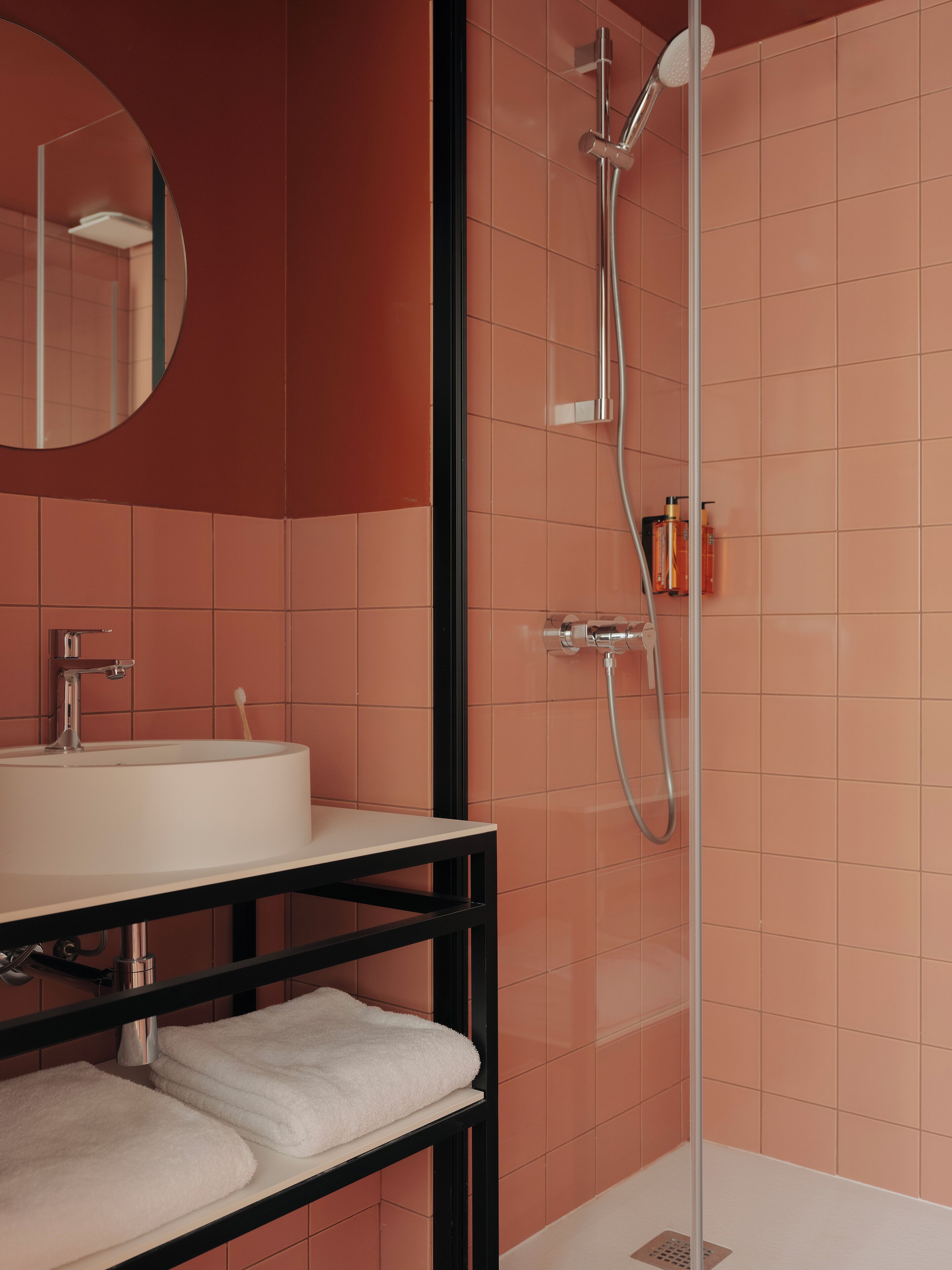 Une salle de bain moderne avec un lavabo blanc, un miroir et une douche équipée d’un pommeau de douche à main.