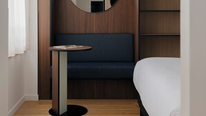 Une chambre d’hôtel moderne avec un mur d’accent en bois, un miroir rond, une petite table ronde, un canapé bleu et un lit avec une literie blanche.