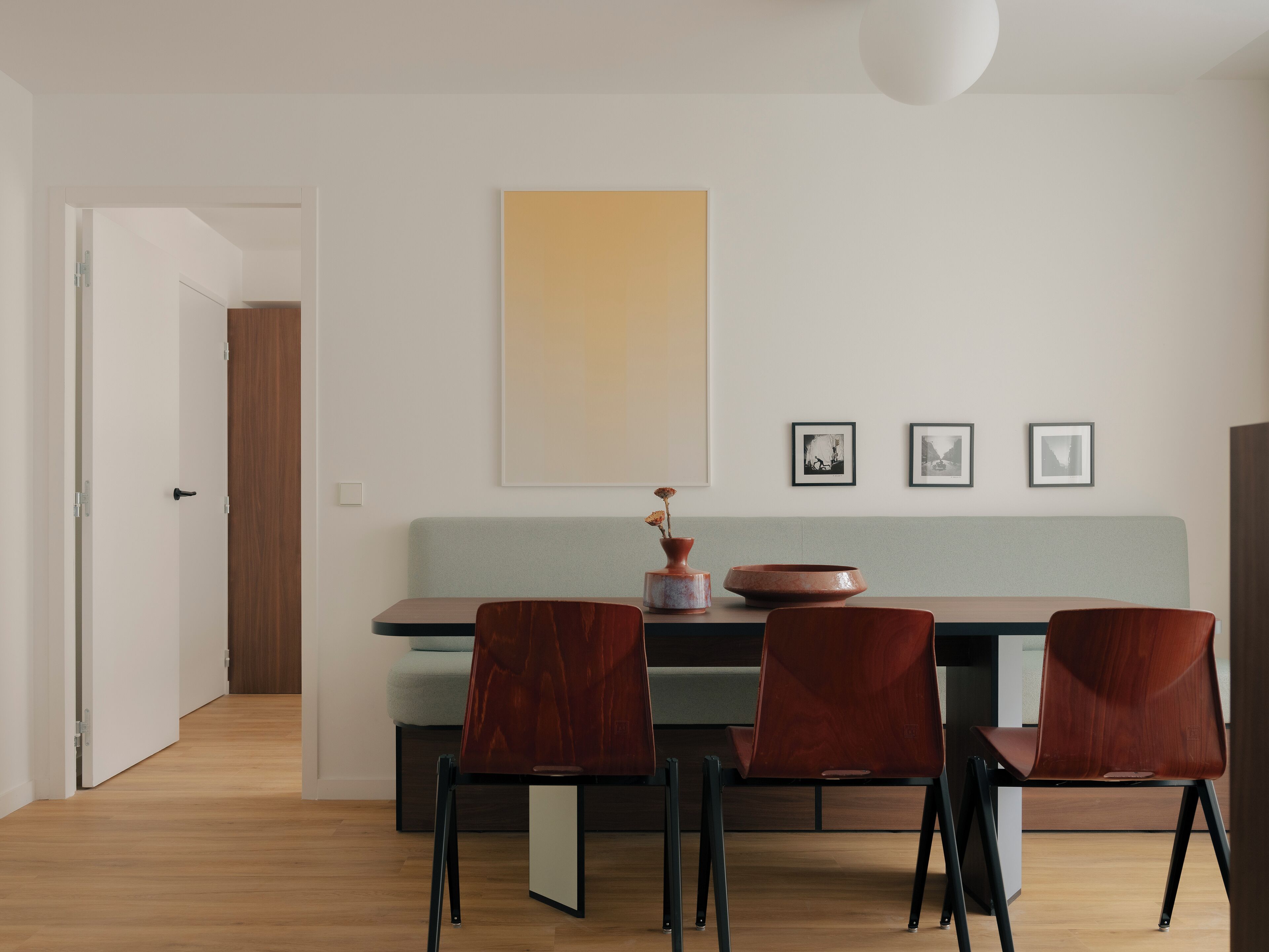 A modern dining area with a wooden table, four chairs, and a large abstract painting on the wall.
