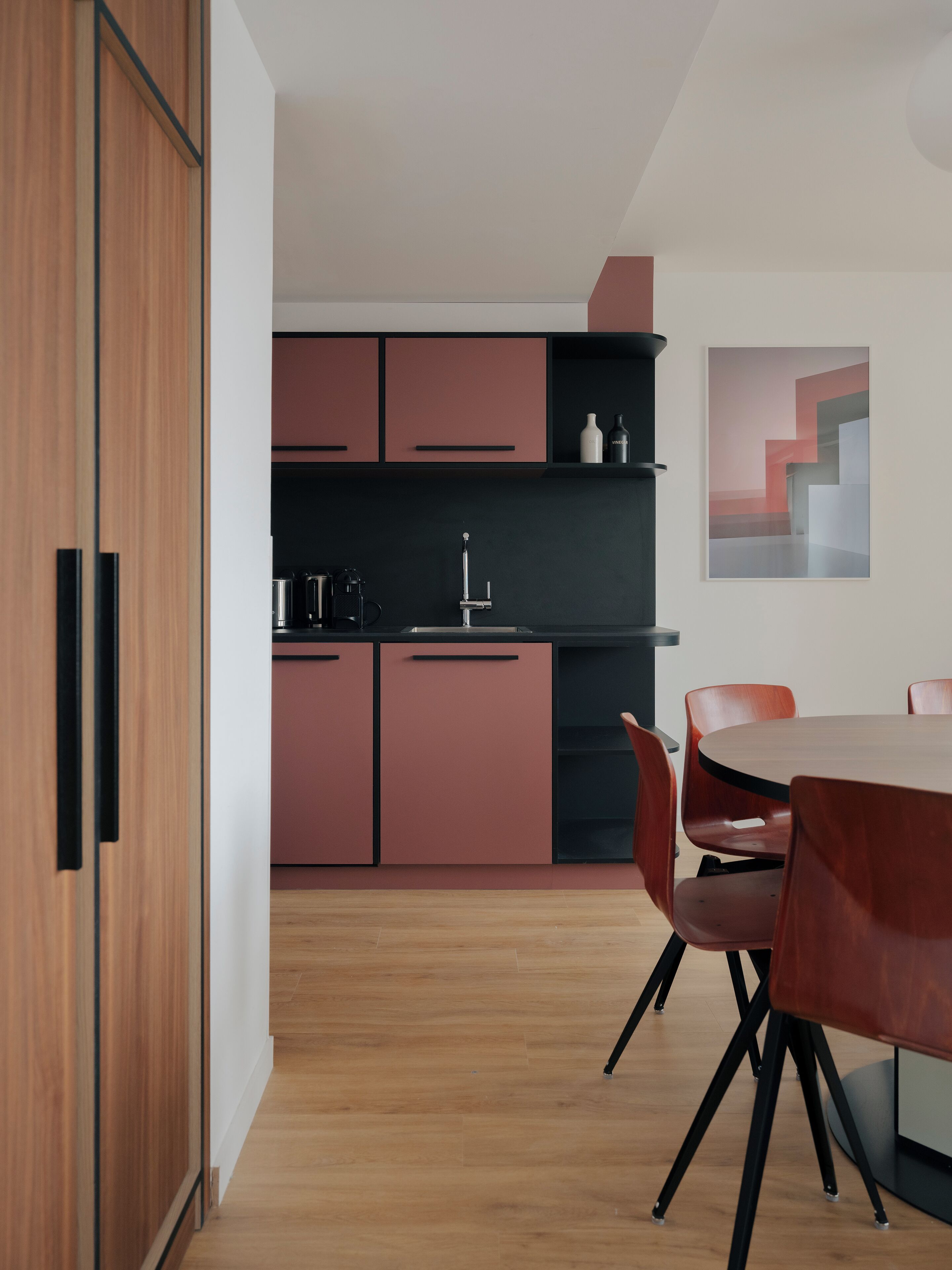 Une cuisine moderne avec des meubles en bois, un plan de travail noir et un coin repas comprenant une table ronde et des chaises.