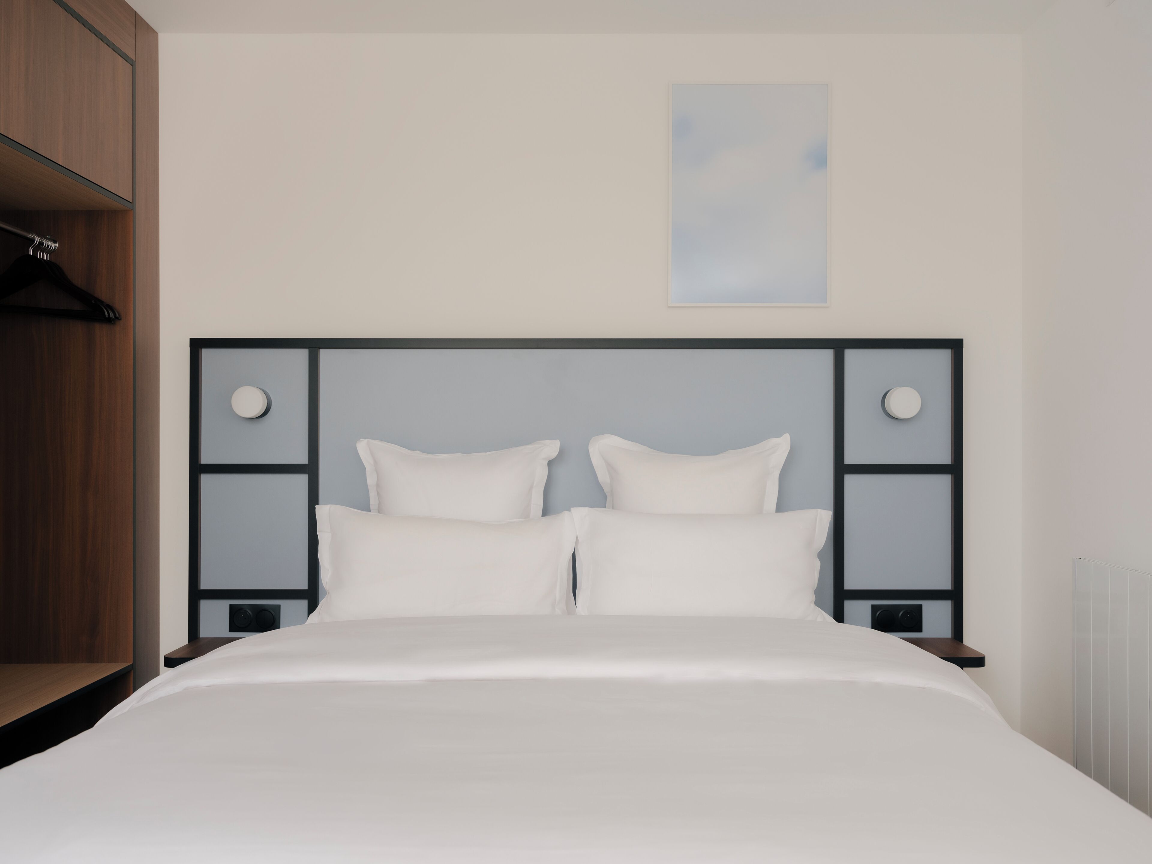 A bed with a white mattress and pillows, a wooden wardrobe, and a framed picture on the wall.