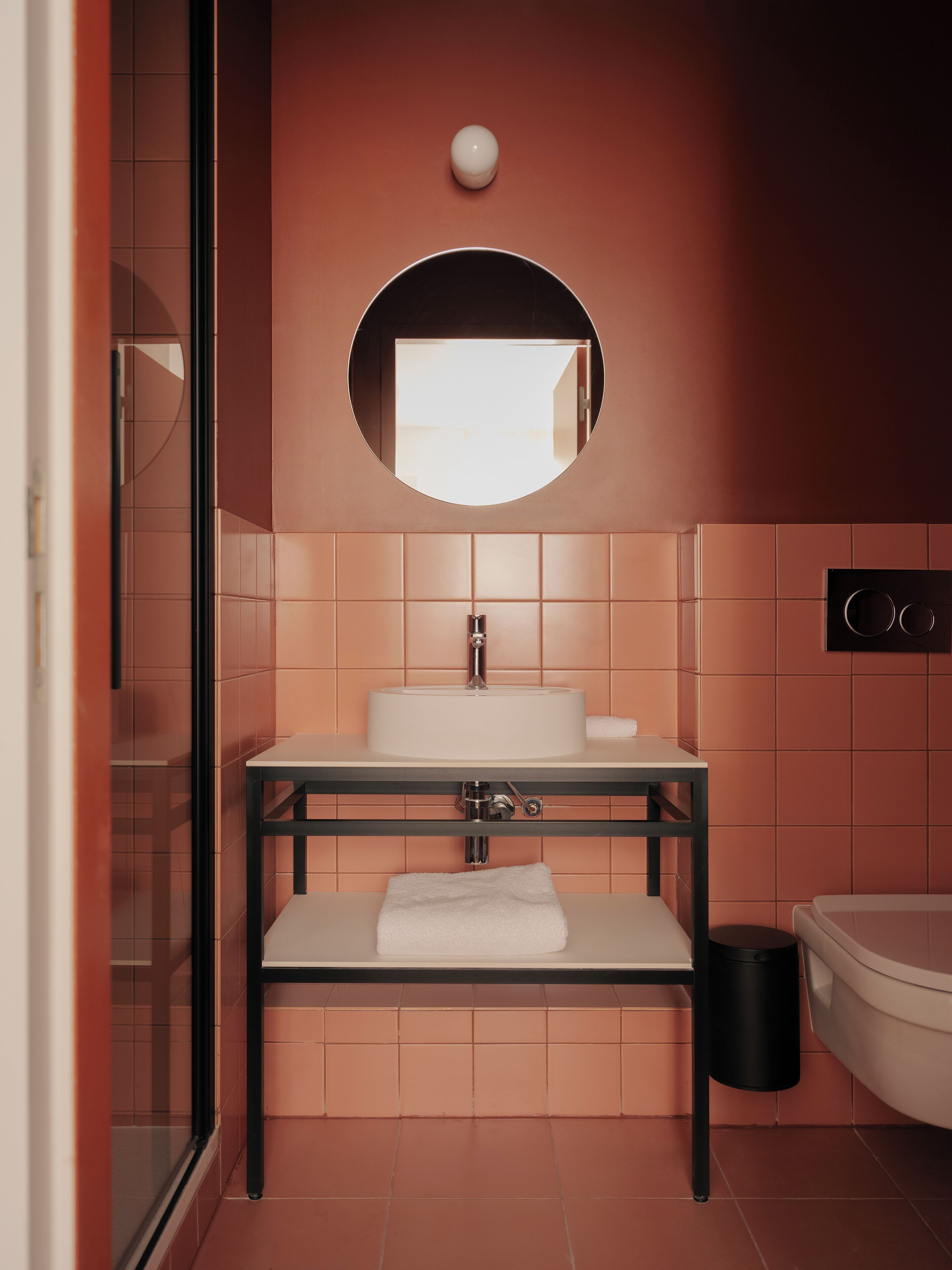 A modern bathroom with a round mirror, white sink, and a towel on the counter.