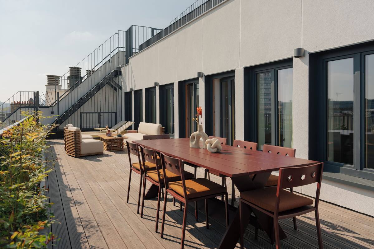Une terrasse sur le toit dotée d’une plateforme en bois, de sièges extérieurs et d’un escalier menant à un niveau supérieur.