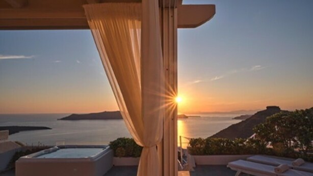 Un balcón con vistas a la puesta de sol sobre el mar, una bañera de hidromasaje y sillones de descanso.